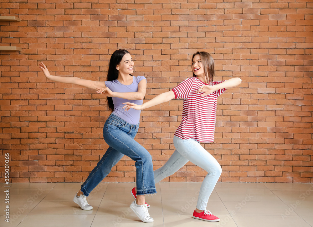 Beautiful young women dancing near brick wall