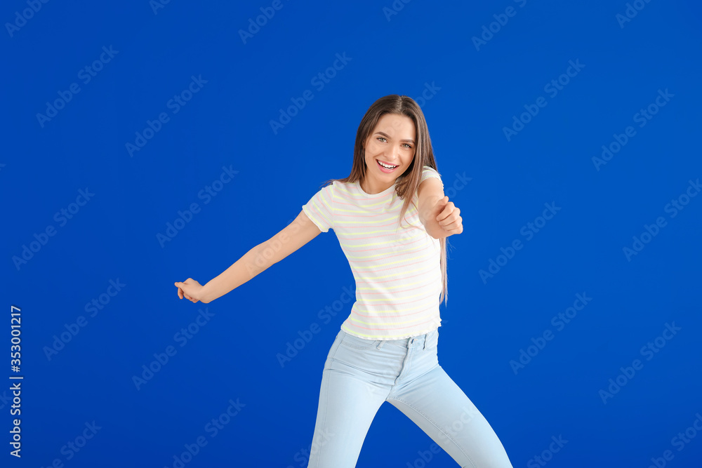 Beautiful young woman dancing against color wall