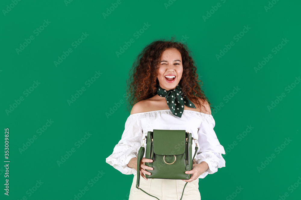 Beautiful young African-American woman with stylish bag on color background