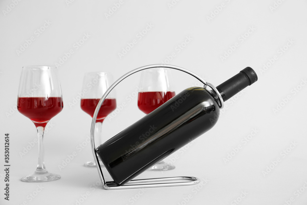 Holder with bottle and glasses of wine on grey background