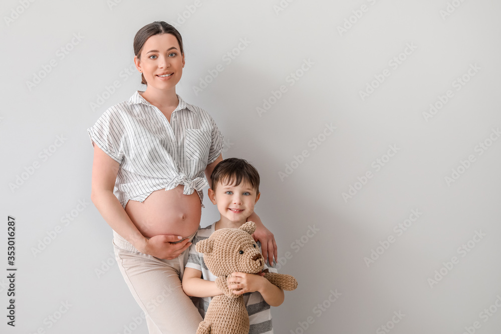 Beautiful pregnant woman with her little son on light background