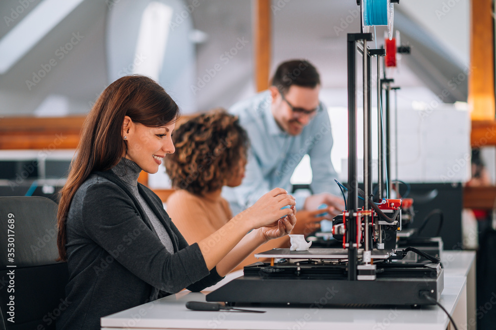 Beautiful smiling woman using 3D printer, side view, portrait.