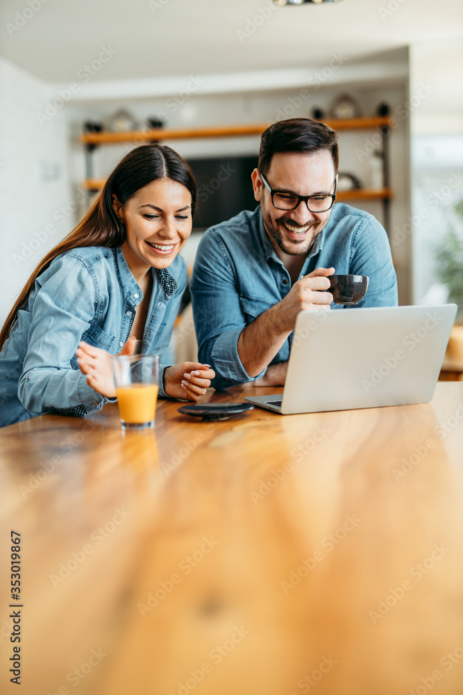 Happy casual couple sitting at table drinking coffee and juice and looking at laptop, portrait.