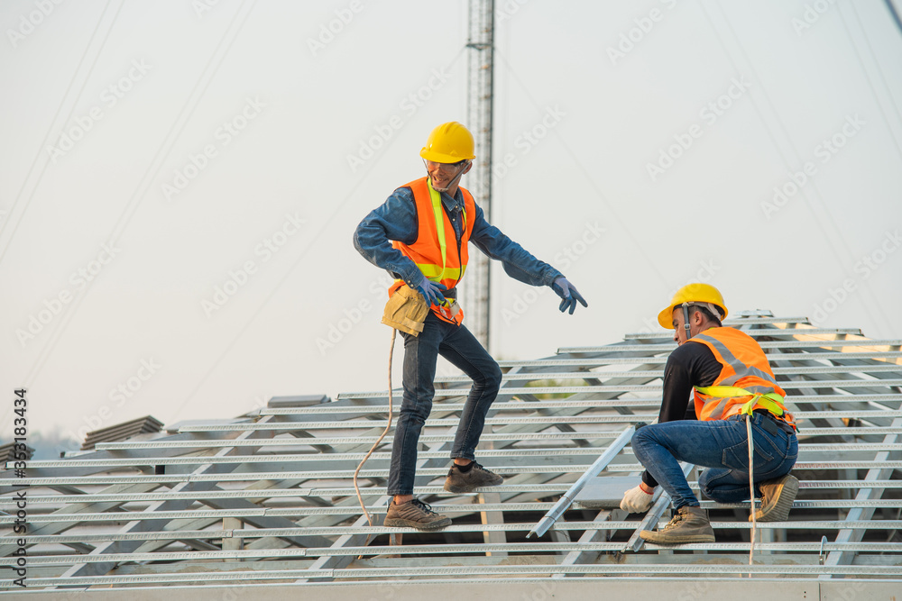 Roofer worker in special protective workwear and gloves installing new roof under construction resid