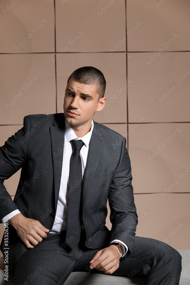 Handsome young man in elegant suit sitting on bench indoors