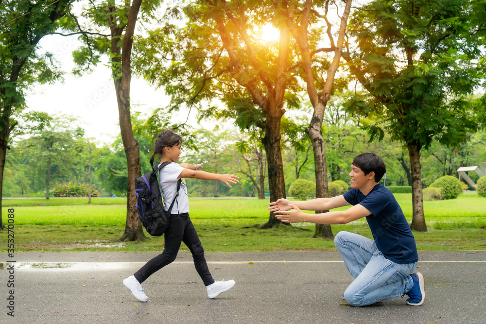 Asian girl preschool student running into father’s hands to hug her after back to school in front of