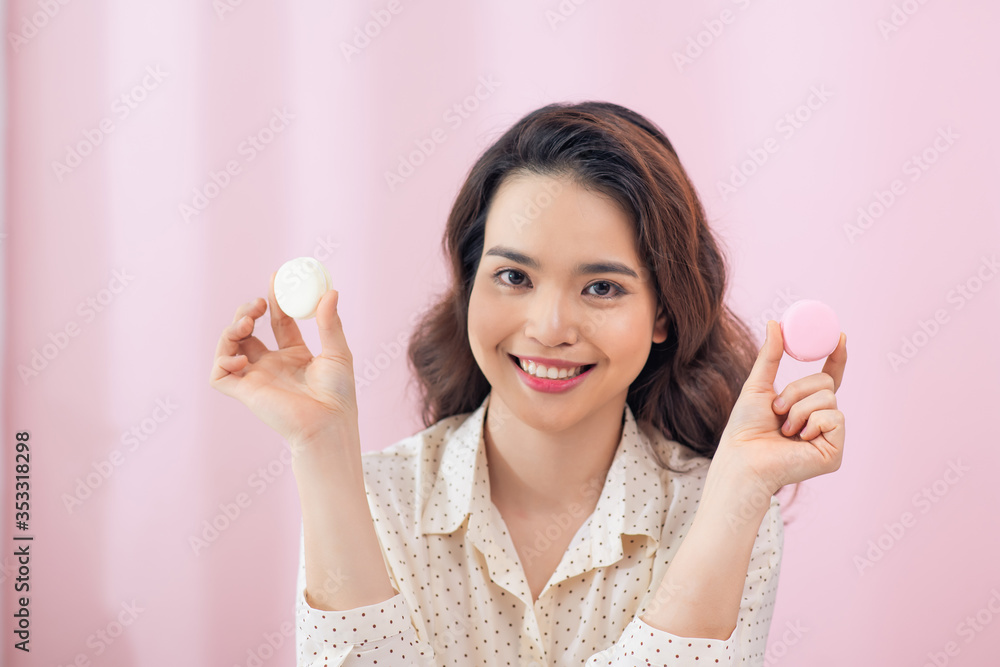 Close up young Asian woman eat cake macarons against pink background.