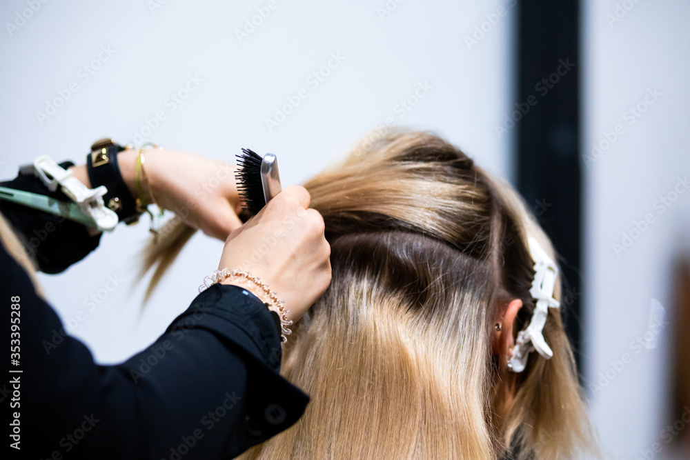 Professional hairdresser making hair extensions for blonde girl in a beauty salon