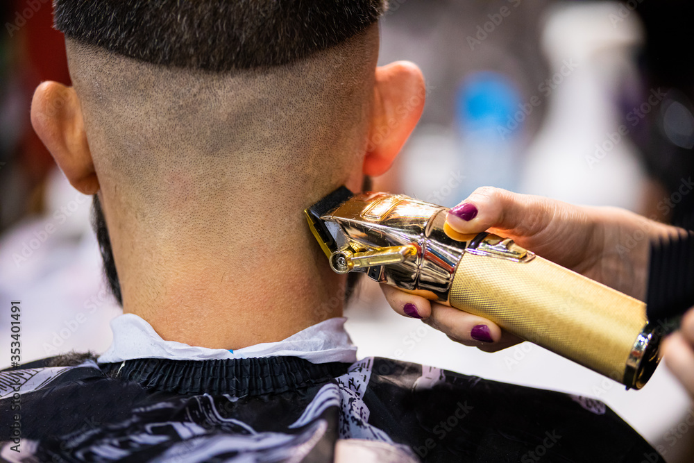 Barber woman cutting client hair to perfect shape using professional trimmer, close up view