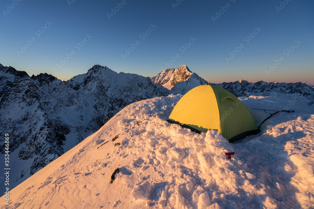 雪山顶上黄色帐篷的日落景观。冬季露营或高山露营