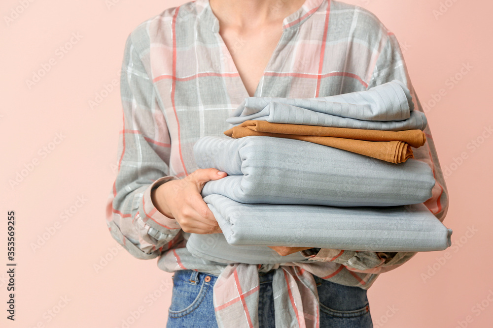 Woman holding stack of clean bed sheets on color background