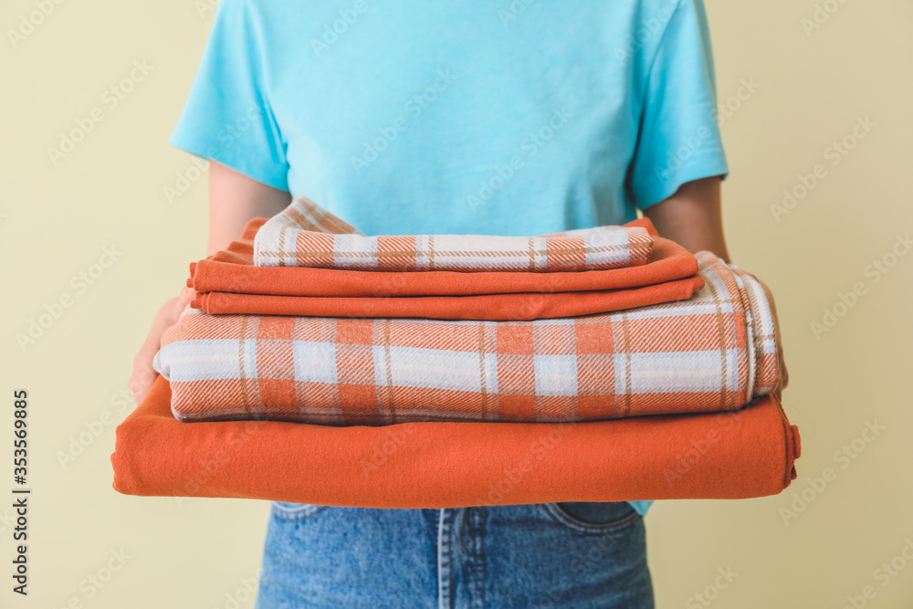 Woman holding stack of clean bed sheets on color background