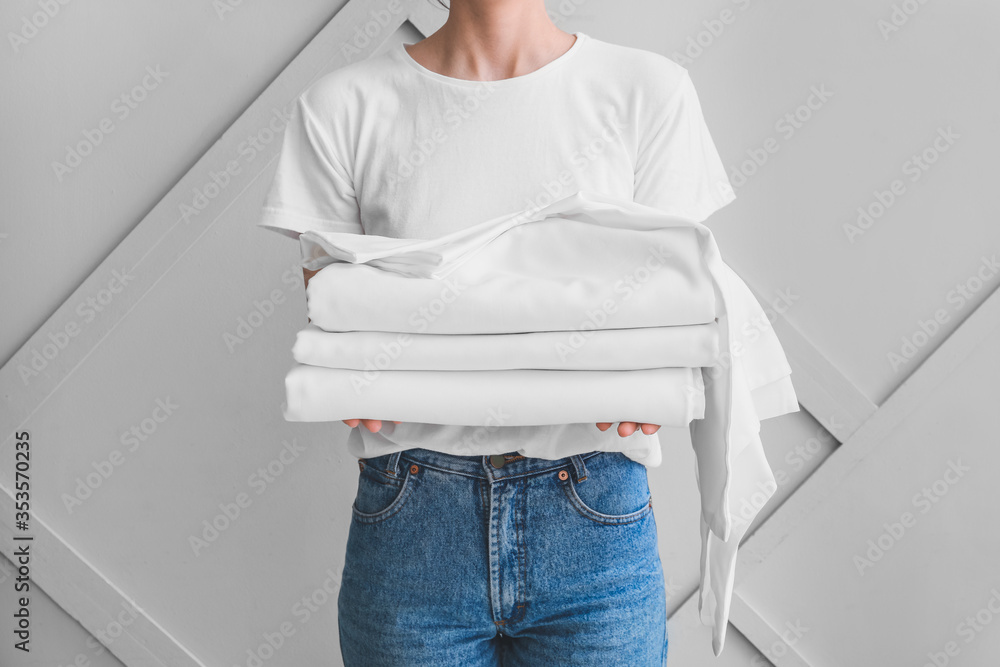 Woman with stack of clean bed sheets on light background