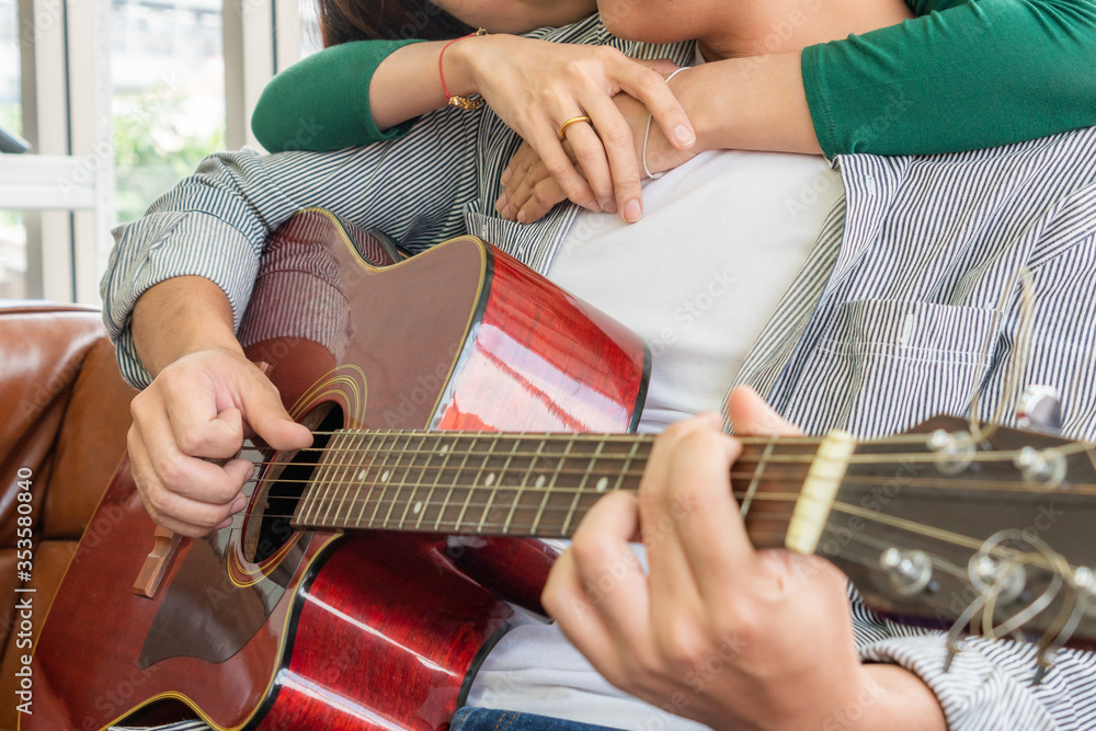 Young Asian Couple Plays Guitar and Sing Song in Living Room at Home Together. Music and Lifestyle c