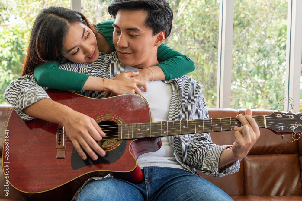 Young Asian Couple Plays Guitar and Sing Song in Living Room at Home Together. Music and Lifestyle c