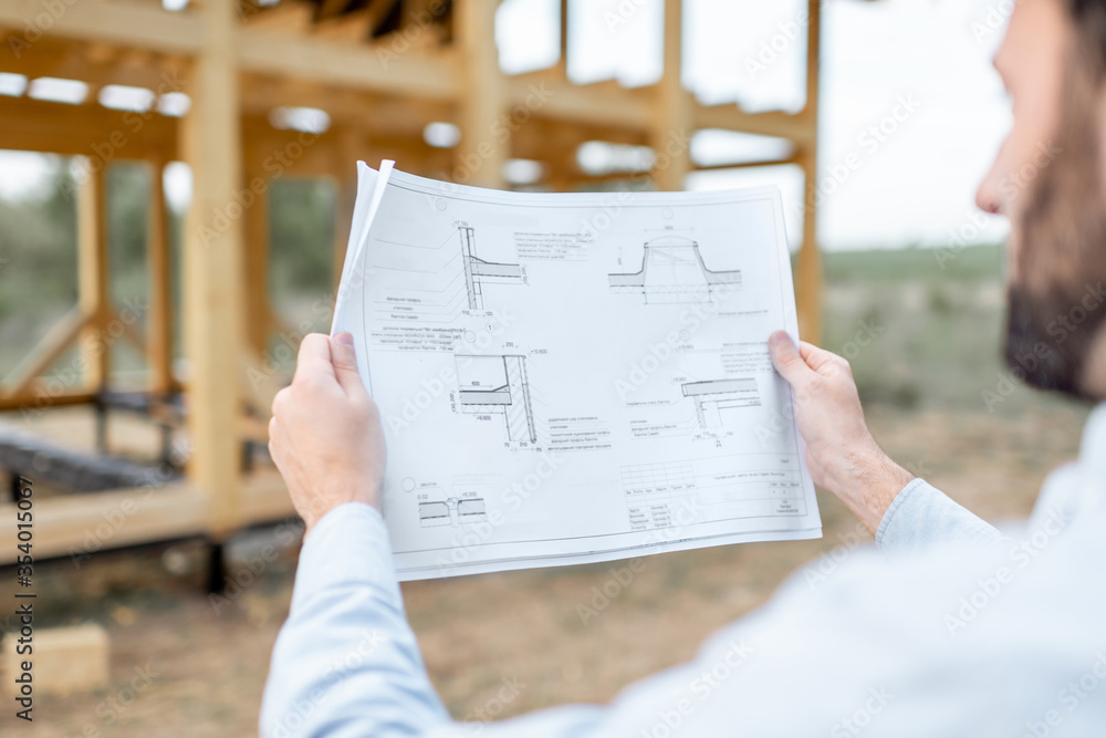 Builder looking on teh drawings of wooden house structures on the construction site. Concept of buil