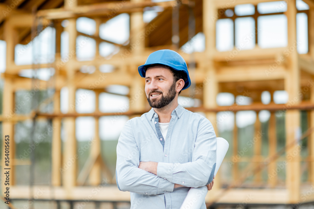 戴着安全帽的建筑师或建筑工人站在木屋结构前的肖像。Bui