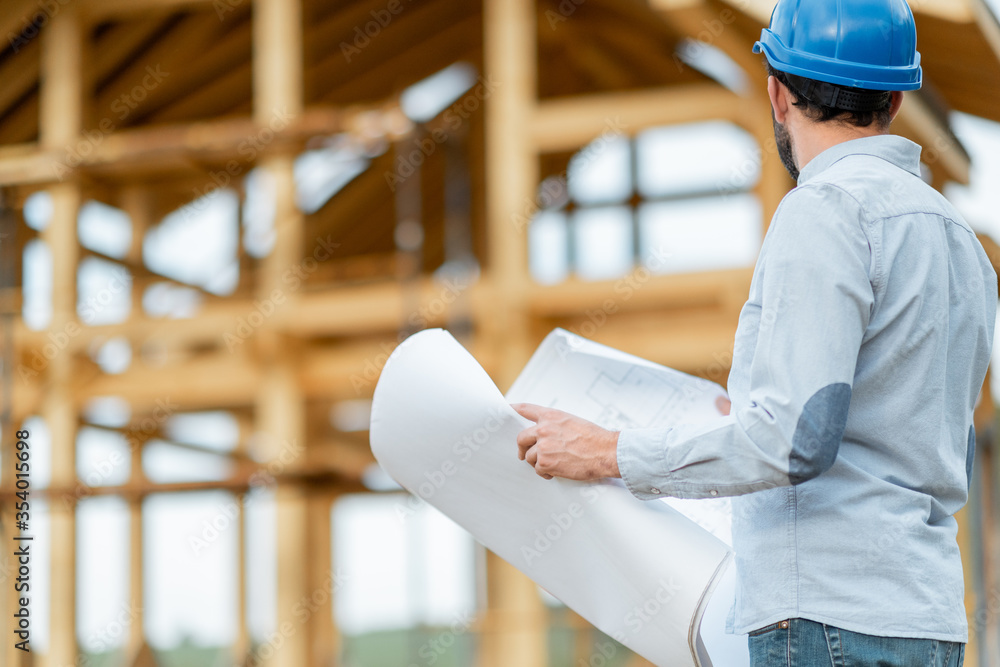 Builder or architect in hard hat supervising a project, standing with blueprints on the construction