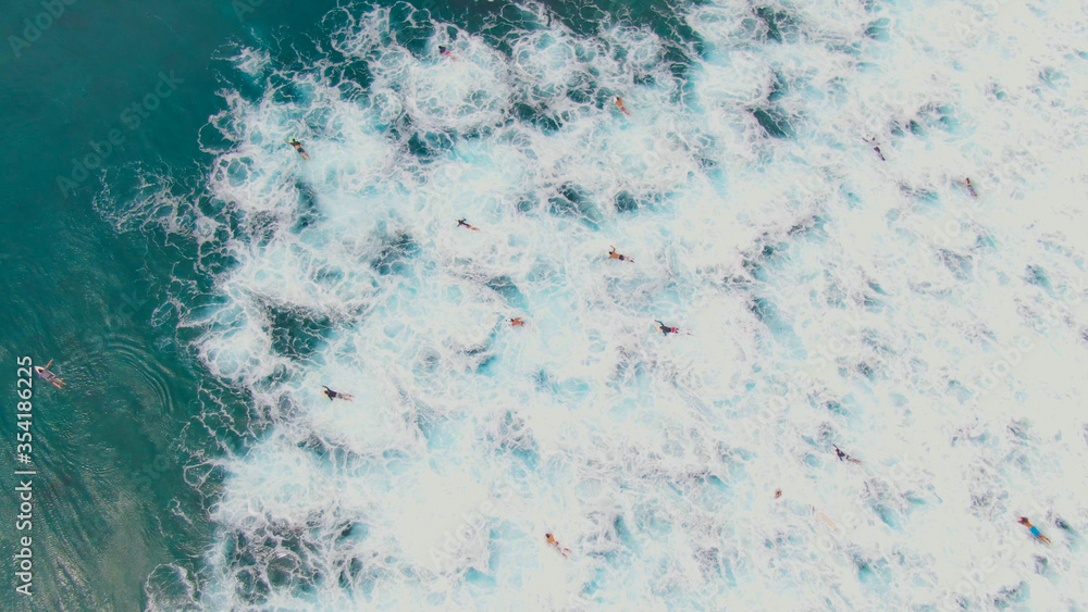 AERIAL: Surfers paddle out to the line up through the foaming ocean water.