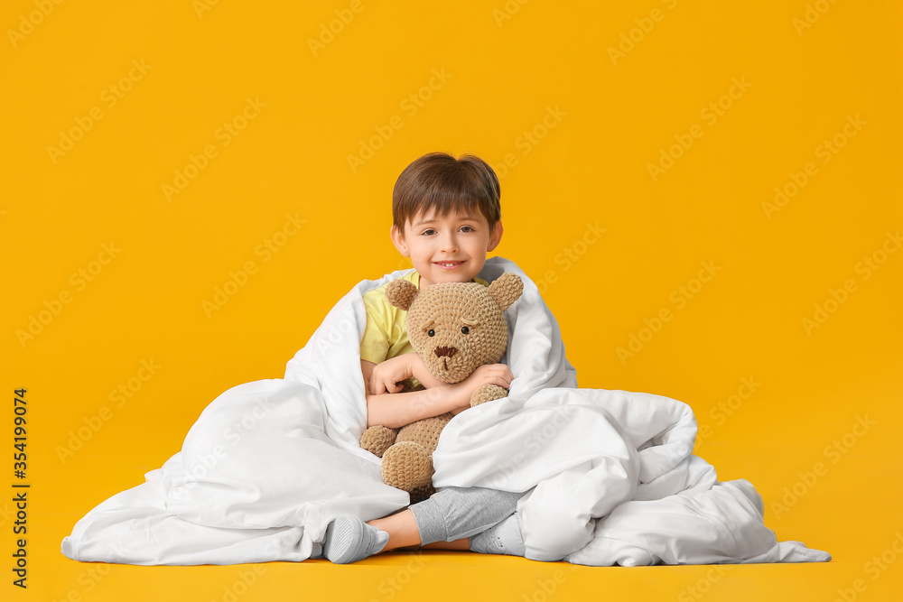 Little boy wrapped in blanket and with toy on color background