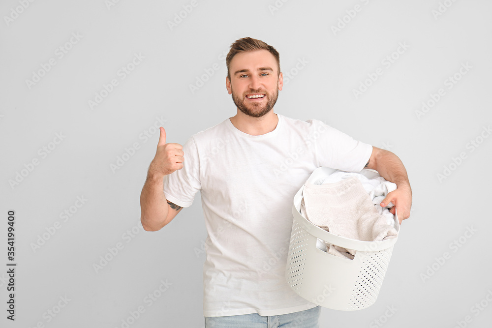 Young man with laundry showing thumb-up gesture on grey background