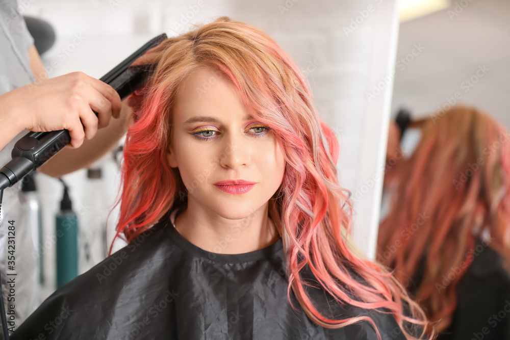 Female hairdresser doing hair of beautiful young woman in salon