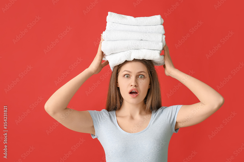 Surprised young woman with clean laundry on color background