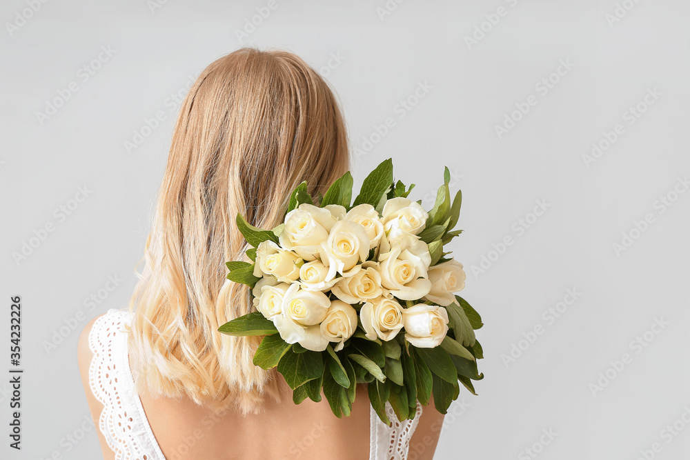 Beautiful young woman with bouquet of roses on light background