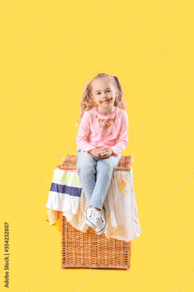 Little girl in dirty clothes eating chocolate on color background