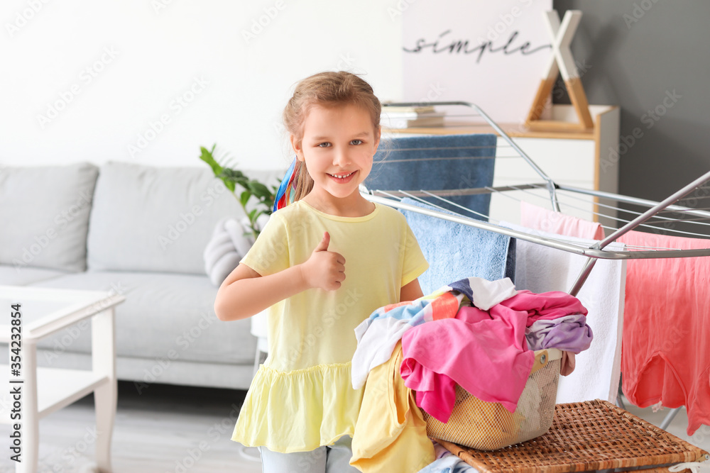 Little girl with dirty laundry showing thumb-up at home