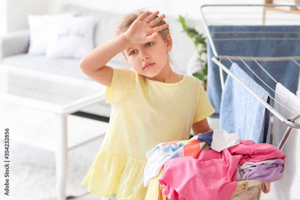 Tired little girl with dirty laundry at home