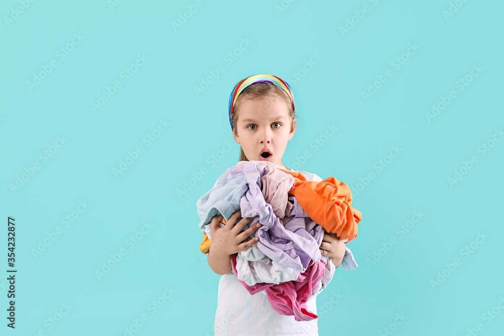 Surprised little girl with dirty laundry on color background