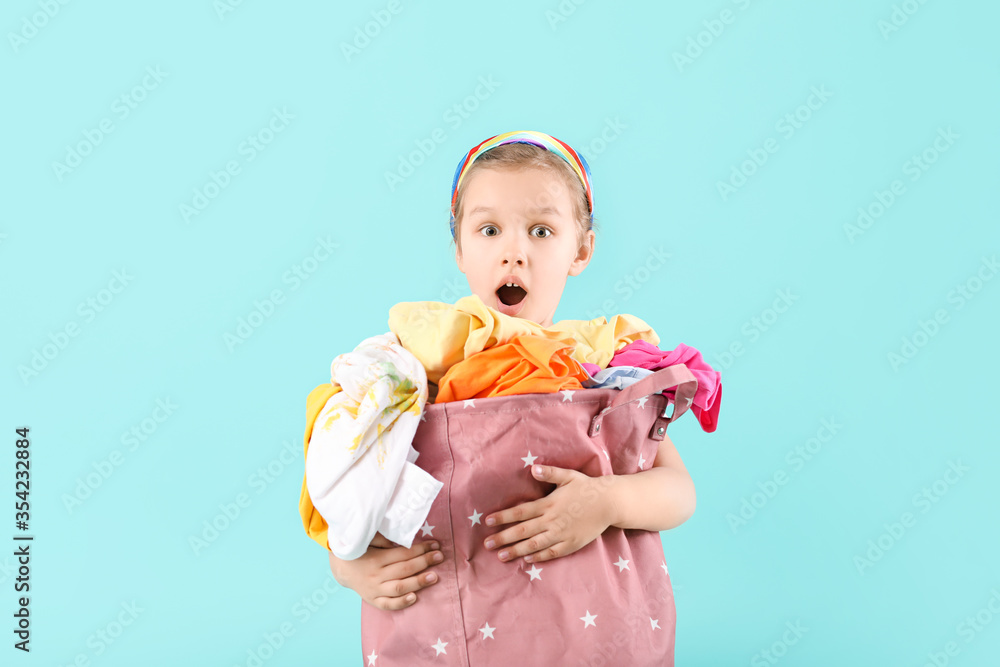 Surprised little girl with dirty laundry on color background