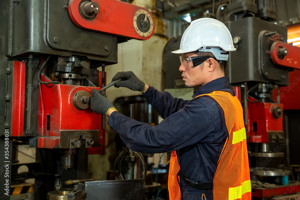 Asian worker in safety hat in machinery room working with machine on the factory.