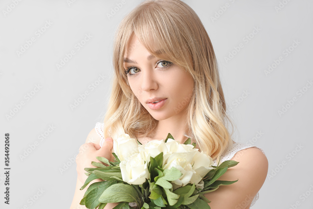 Beautiful young woman with bouquet of roses on light background