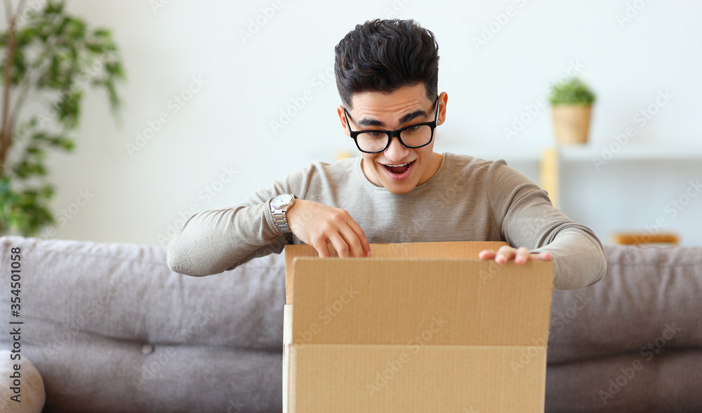 Happy man unpacking delivery box on sofa.