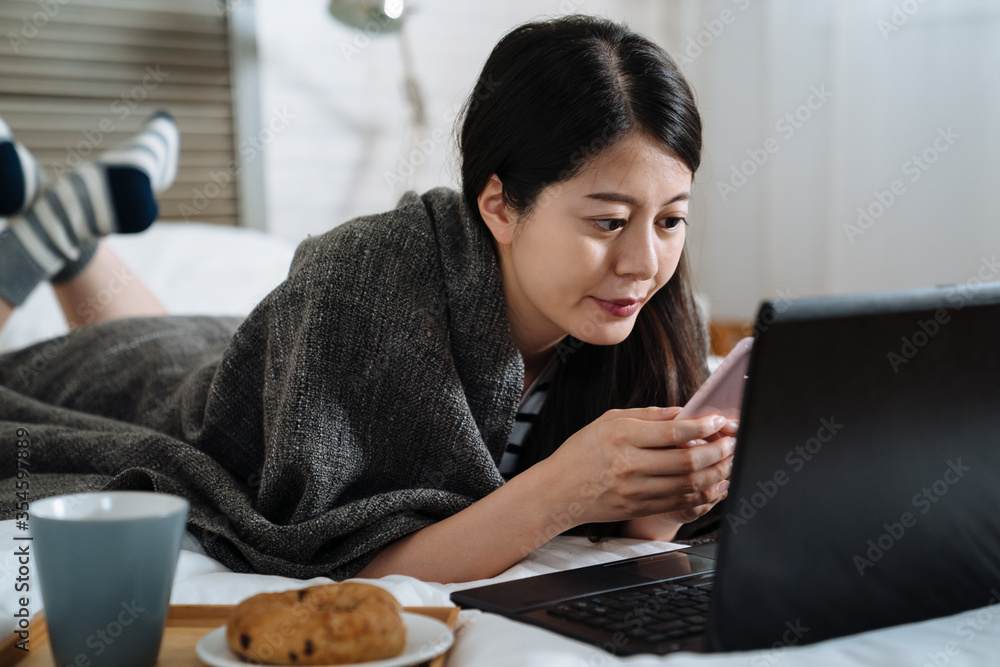 年轻漂亮的微笑女人在床上吃早餐，使用科技手机。亚洲韩国人g