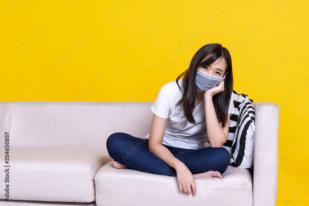 Asian woman wearing medical mask and working from home use laptop computer while sitting on sofa ove