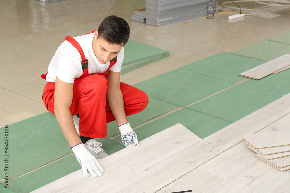 Carpenter installing laminate flooring in room