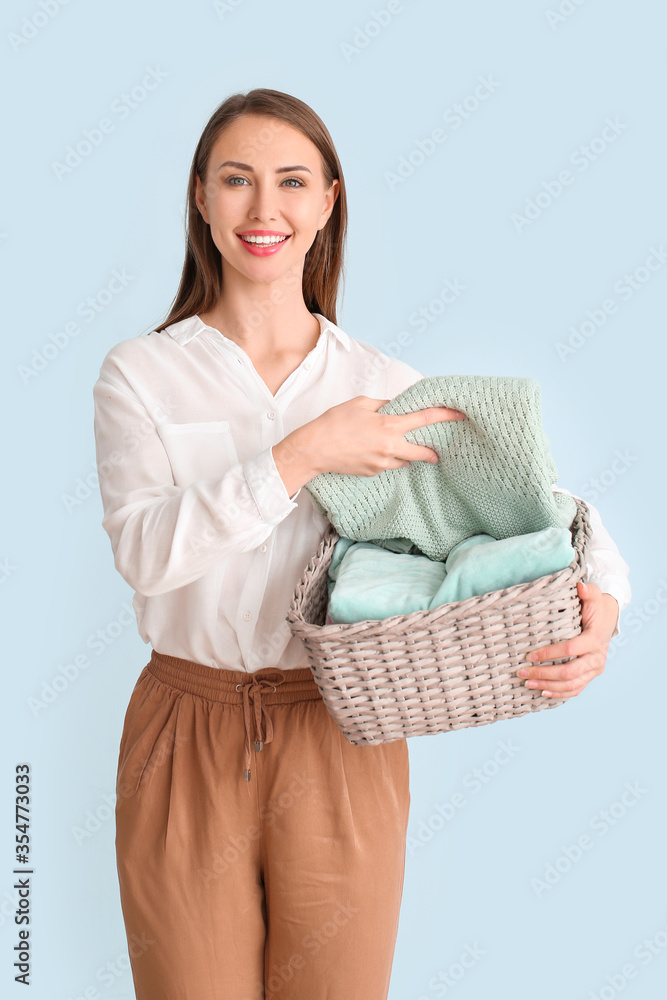 Young woman with clean laundry on light background