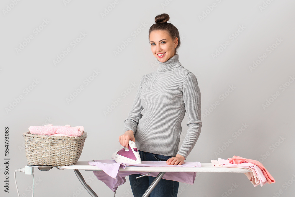 Young woman ironing laundry on grey background