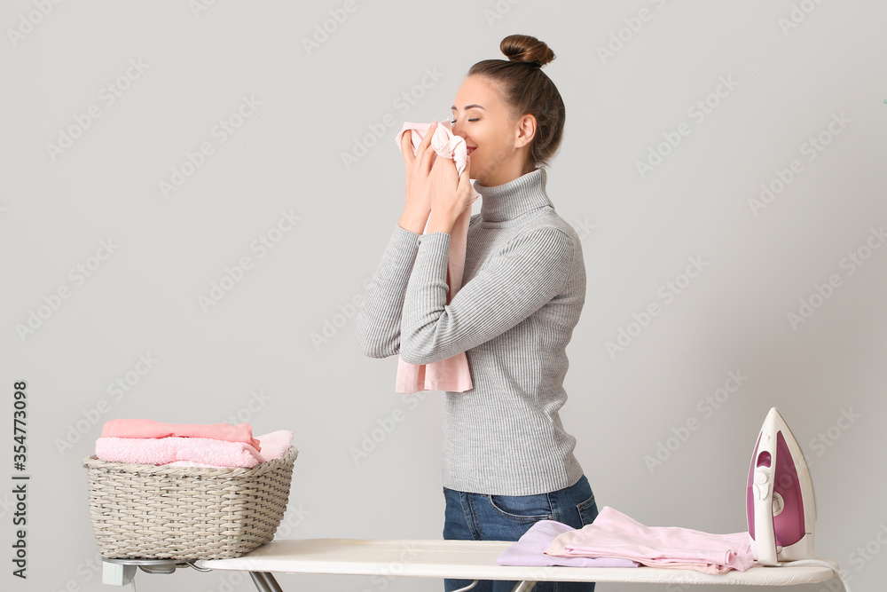 Young woman ironing laundry on grey background