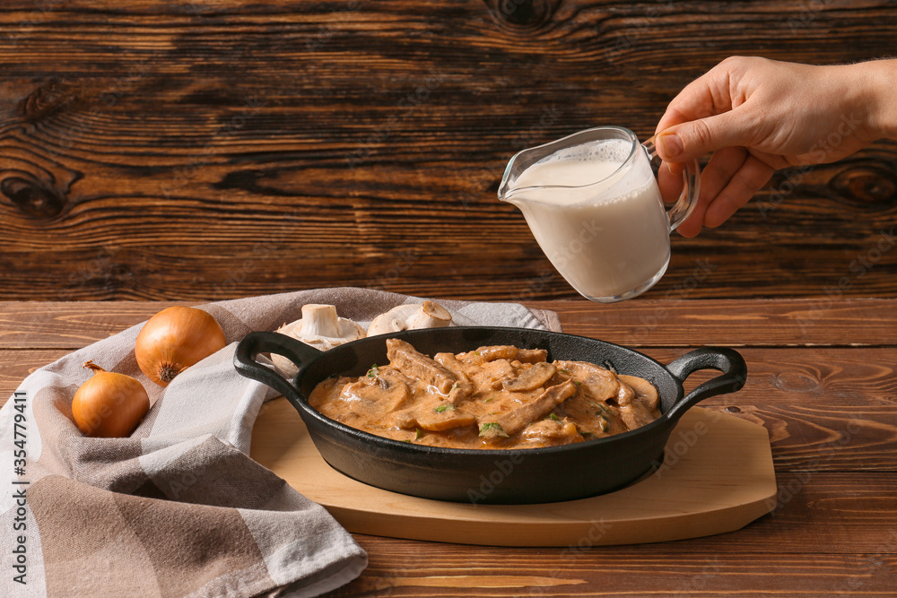 Woman cooking tasty beef stroganoff on table