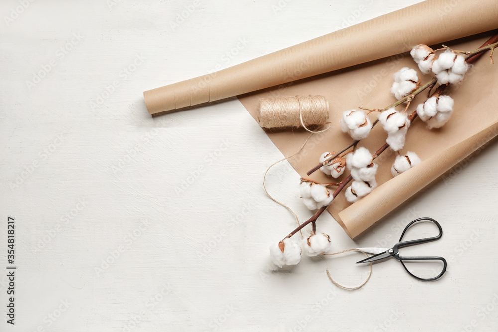 Beautiful cotton flowers, wrapping paper, thread and scissors on white background