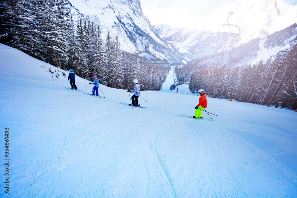 Ski school for kids, group of children ride down the slope one after another with mountains on backg