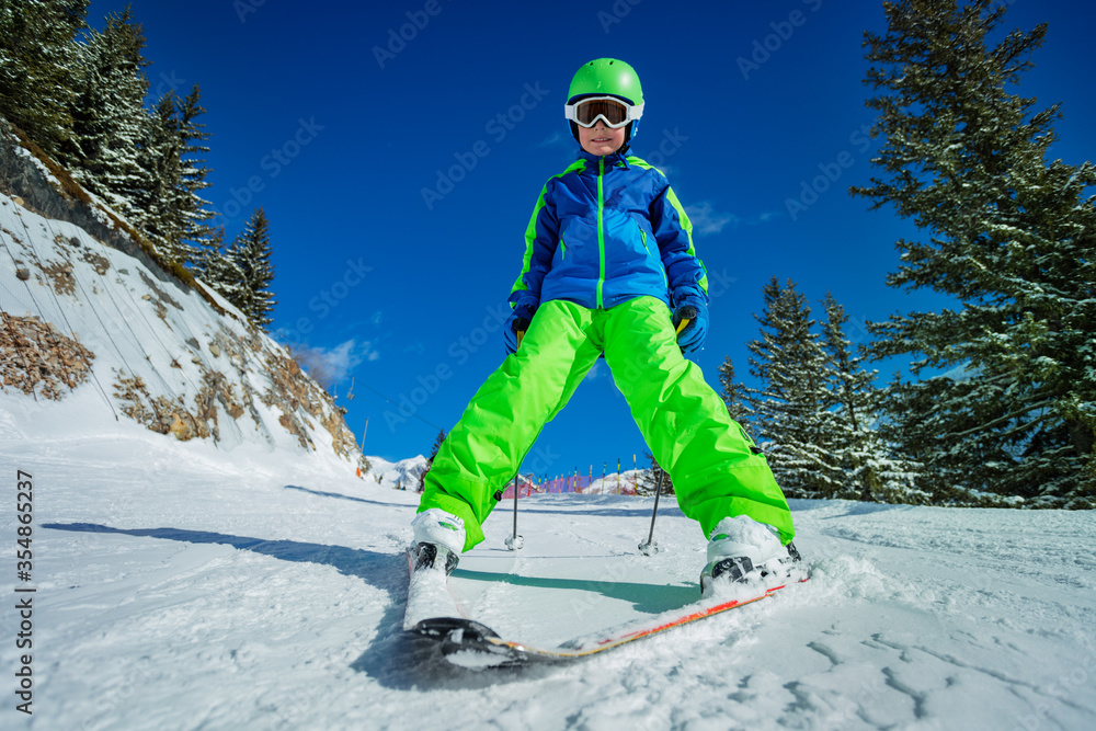 快乐的10岁男孩滑雪者穿着亮绿色衣服学习滑雪的有趣画像