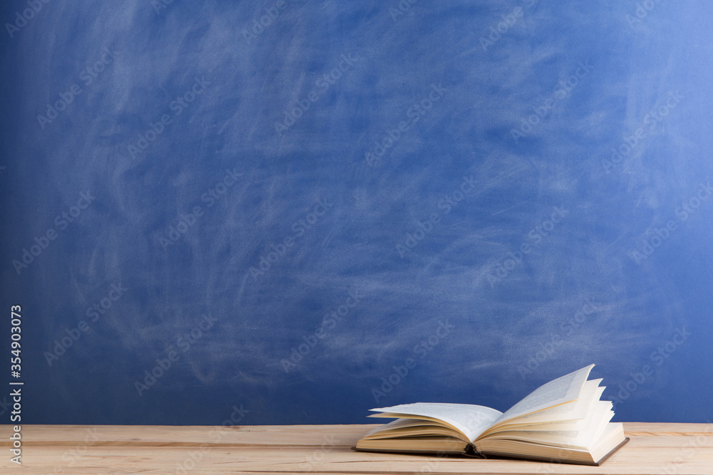 Education and reading concept - group of books on the wooden table, blue blackboard background. Teac