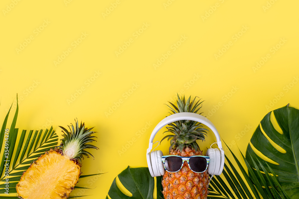 Funny pineapple wearing white headphone, listen music, isolated on yellow background with tropical p