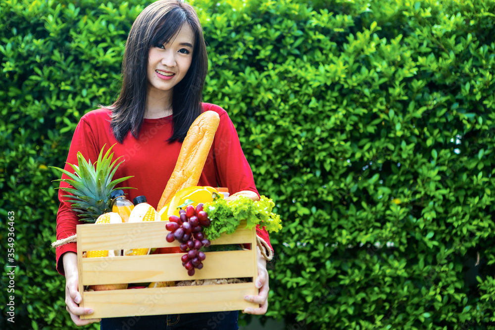 亚洲妇女拿着装有蔬菜的木篮子。篮子里有新鲜蔬菜。在花园野餐