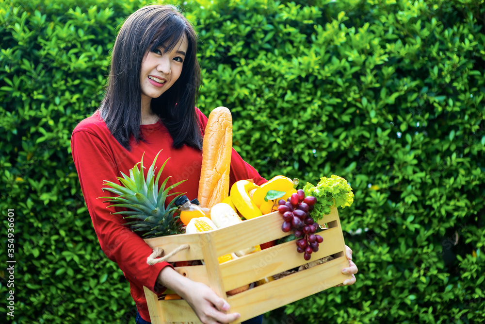 亚洲妇女拿着装有蔬菜的木篮子。篮子里有新鲜蔬菜。在花园野餐